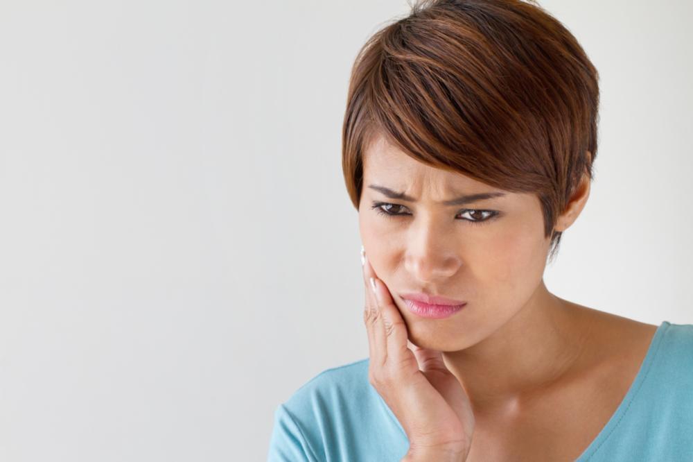 Woman holding her face in pain from tooth sensitivity near 27103 