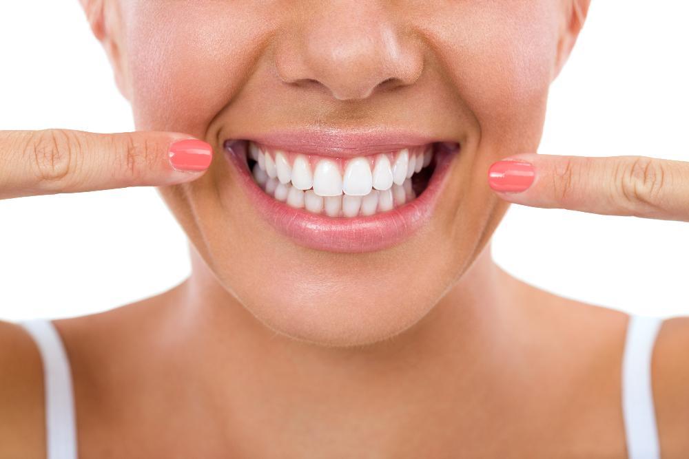 Dental patient smiling and pointing at their healthy teeth & gums in 27103